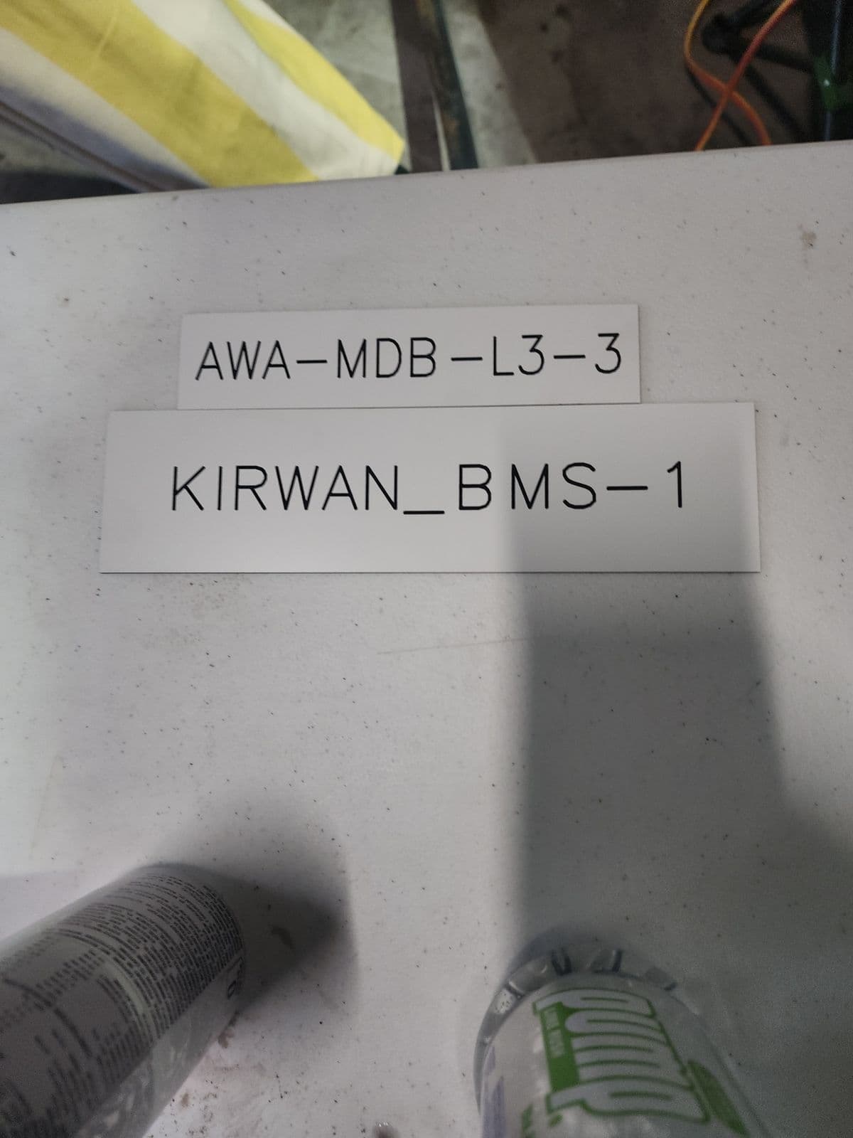 Two white traffolyte board identification tags engraved with board references