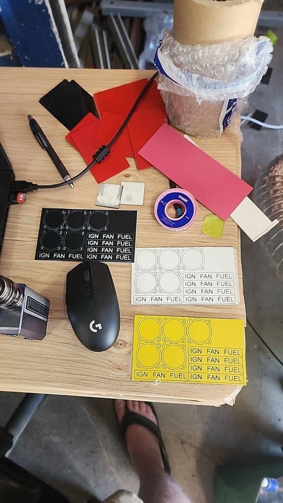 Sheet of laser-cut IGN FAN FUEL selector labels in black, red, pink, white and yellow traffolyte laid out on a workbench