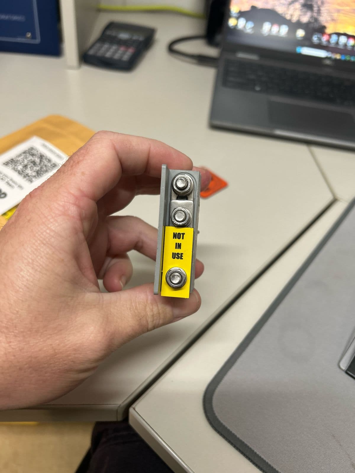Yellow traffolyte Not In Use tag fitted to a small busbar link between two mounting bolts