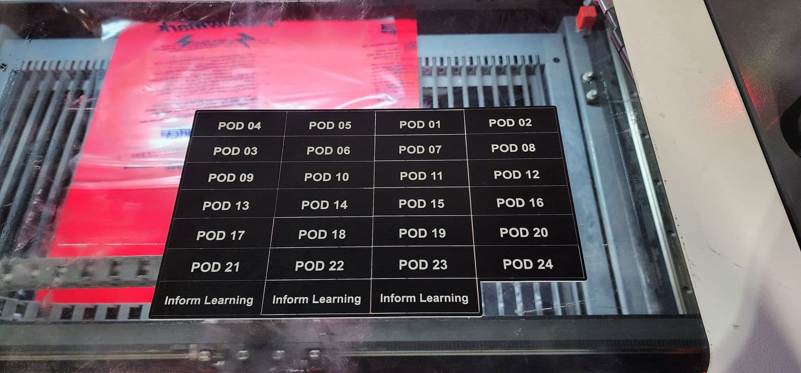 Sheet of black traffolyte tags numbered POD 01 through POD 24 with Inform Learning tags, engraved on a laser bed