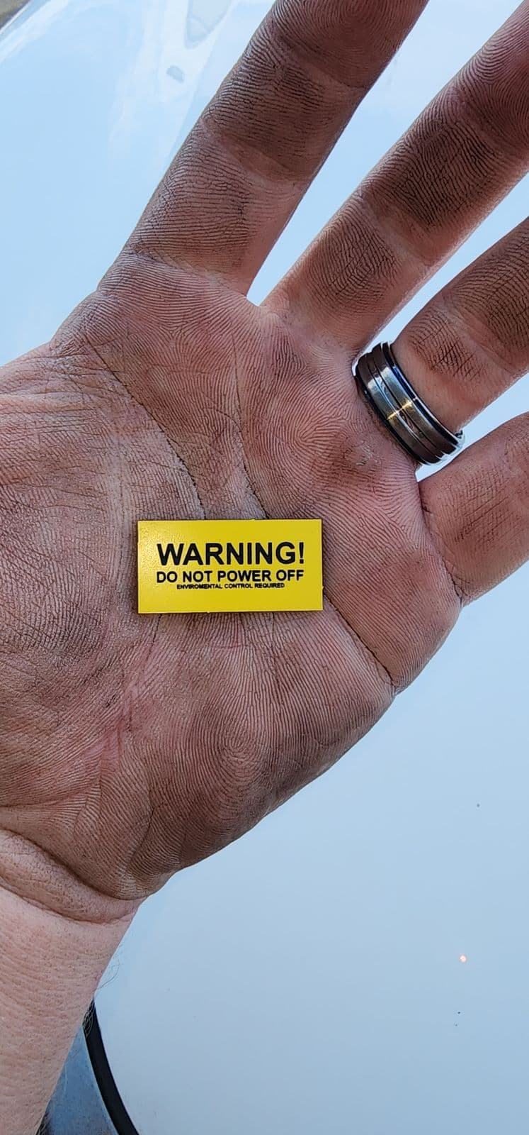 Small yellow traffolyte tag reading WARNING! Do Not Power Off, Environmental Control Required, held in an open palm