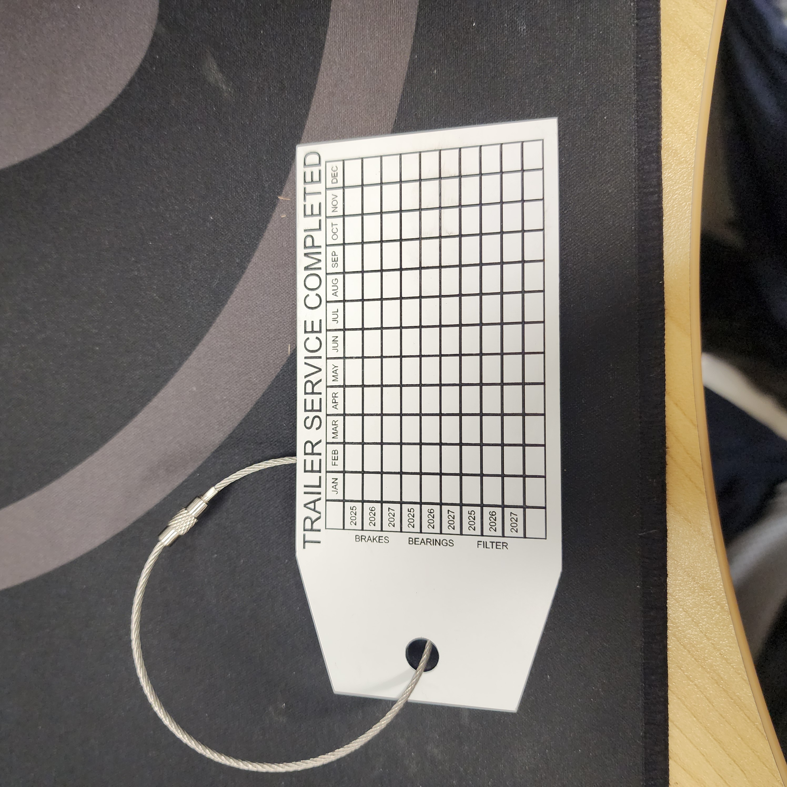 Engraved traffolyte trailer service tag with a maintenance tracking grid, attached with a stainless steel ring
